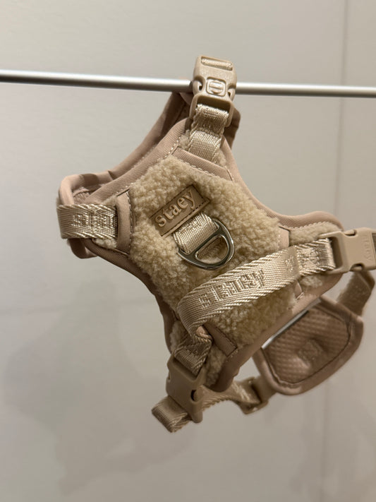 Tan dog harness with metal buckle on a white background