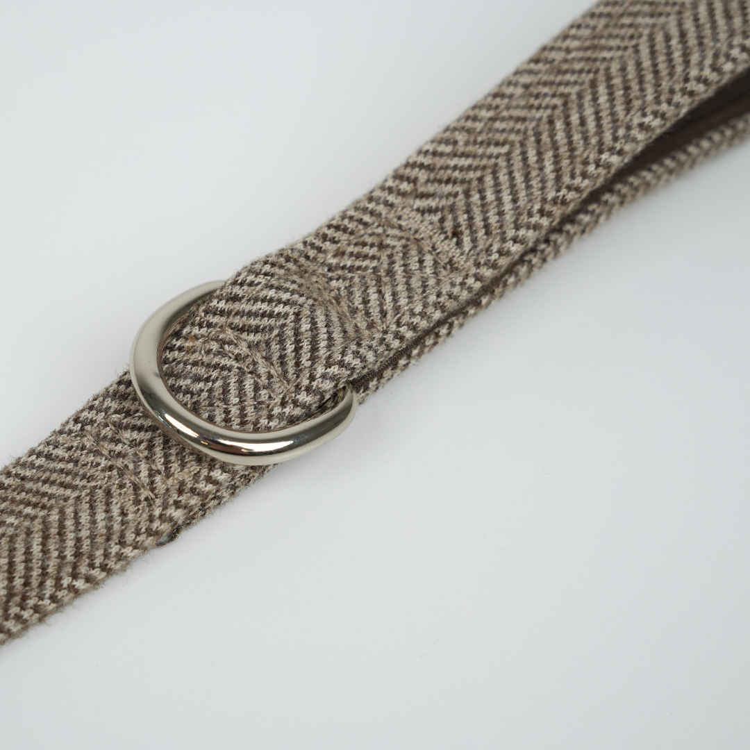 Brown herringbone patterned belt with a silver buckle on a white background
