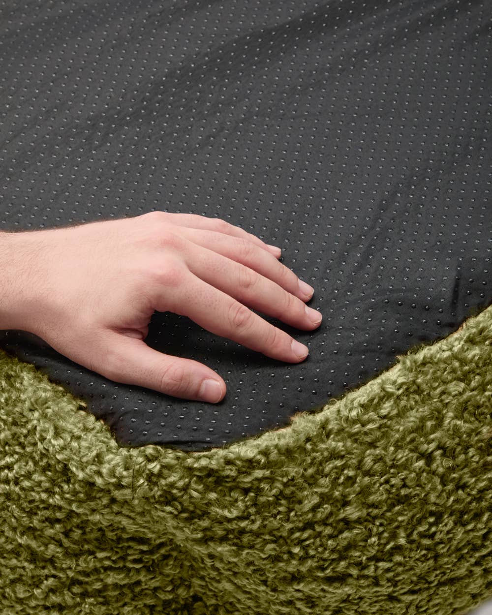 Hand resting on a textured black surface with a green fabric background