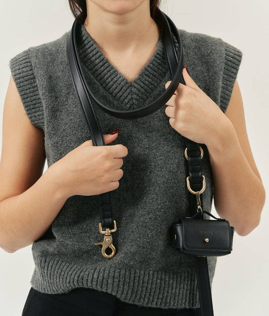 Person holding a black handbag with a strap over their shoulder against a white background