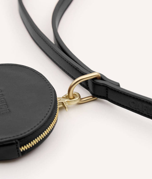 Black circular pouch with gold zipper and strap on a white background