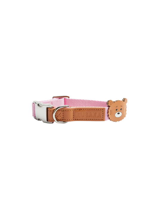 A pink fabric dog collar with a tan leather strap, silver buckle, and a small 3D bear head charm on the side.