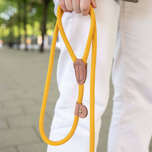 Yellow rope dog leash with brown leather stopper held by a person in white pants outdoors.