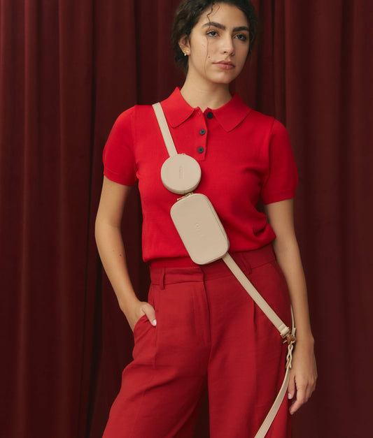 Woman wearing a red outfit with a beige bag against a red curtain background