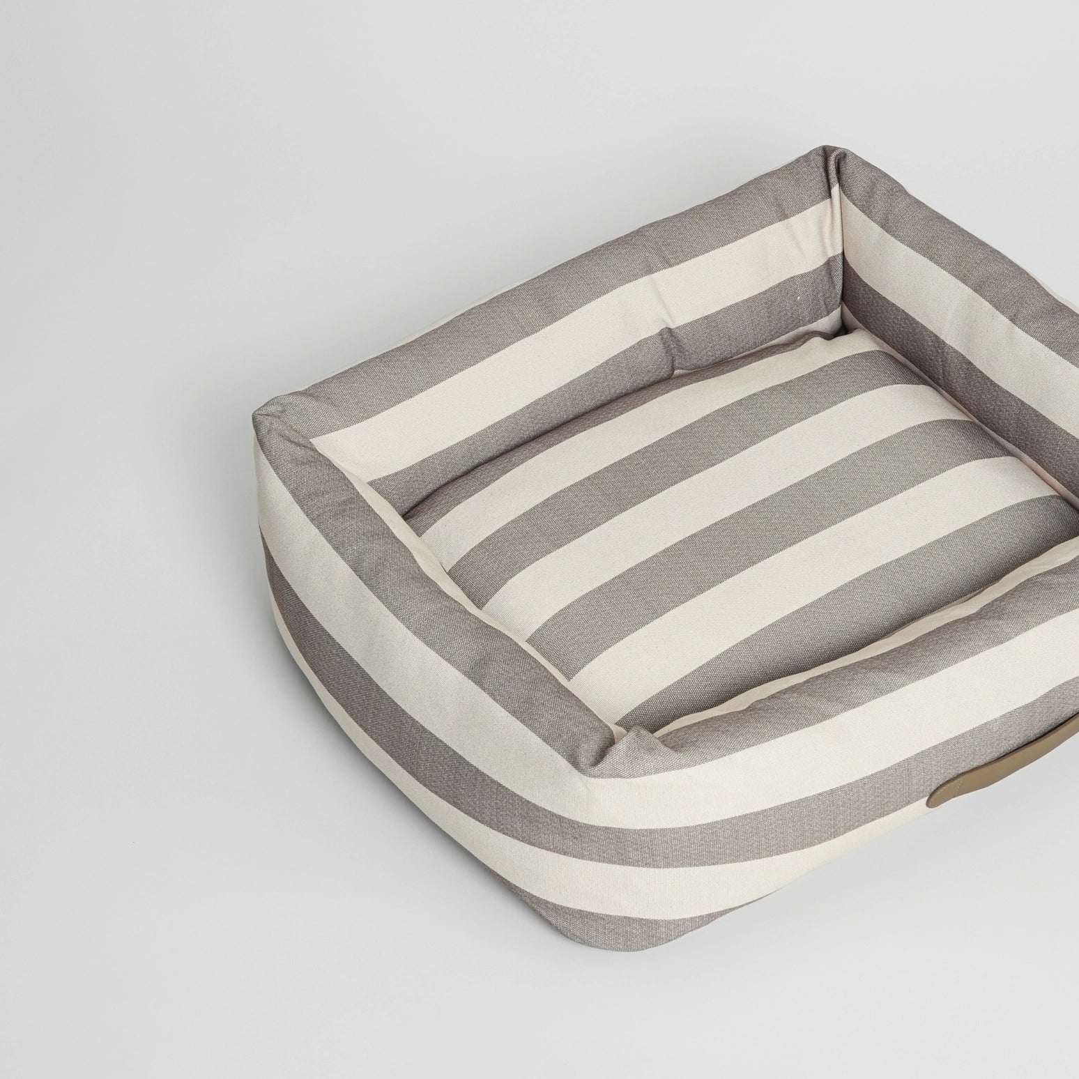 Striped dog bed with a pillow on a light grey background