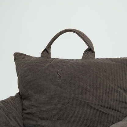 Brown textured pillow with a handle on a light gray background