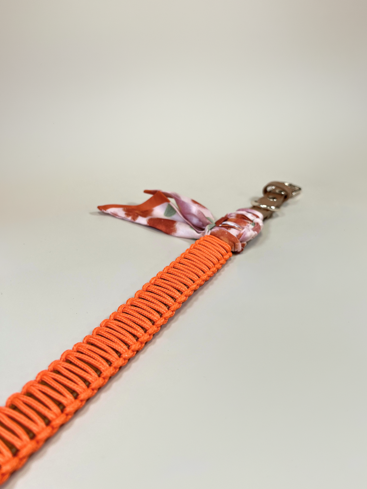 Orange paracord lanyard with a patterned end on a light gray background