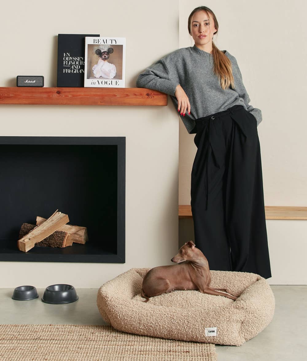 Woman standing next to a dog on a fluffy pet bed in a cozy living room.