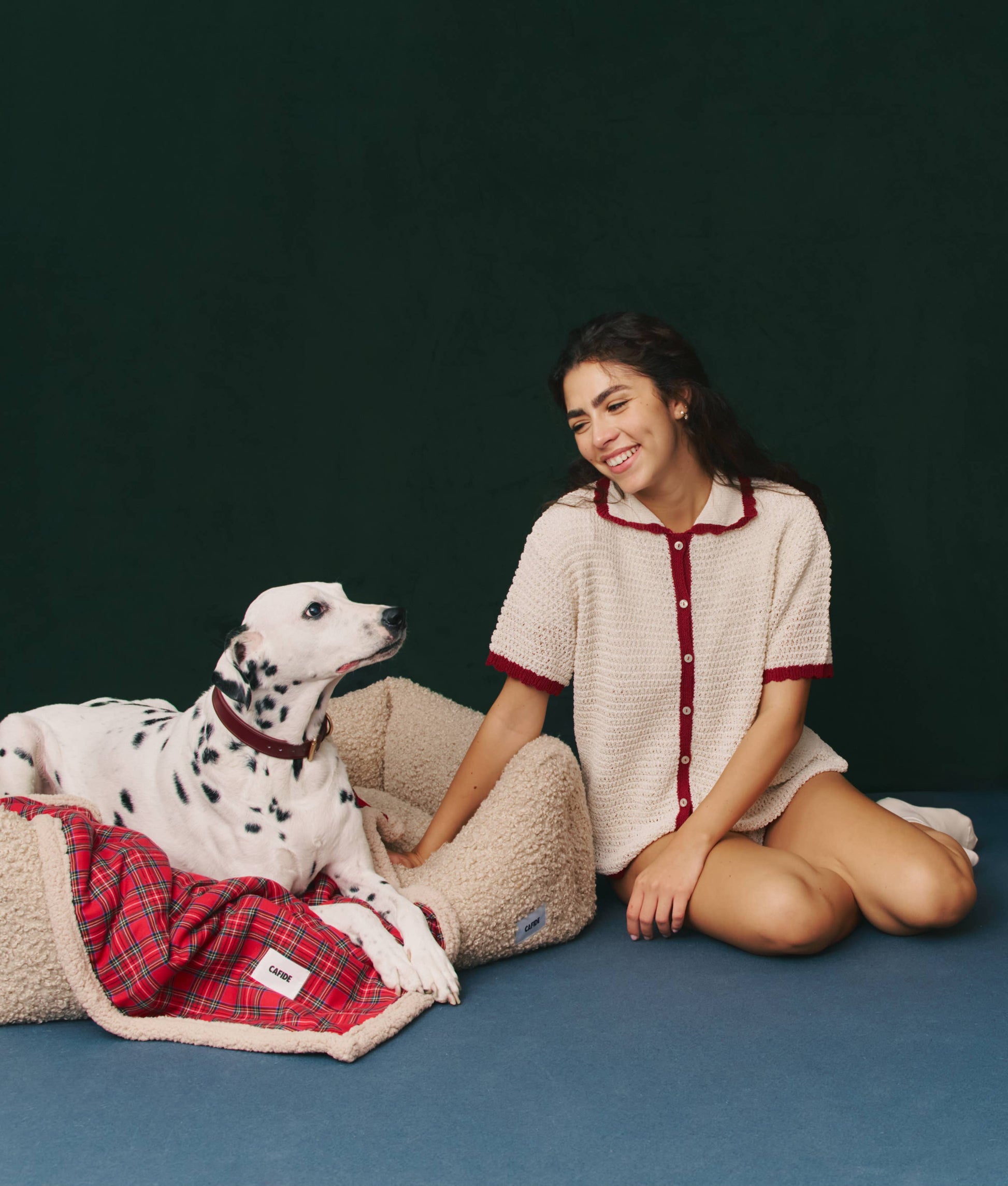 Woman in a white and red outfit sitting next to a Dalmatian dog on a blue floor with a dark green background.