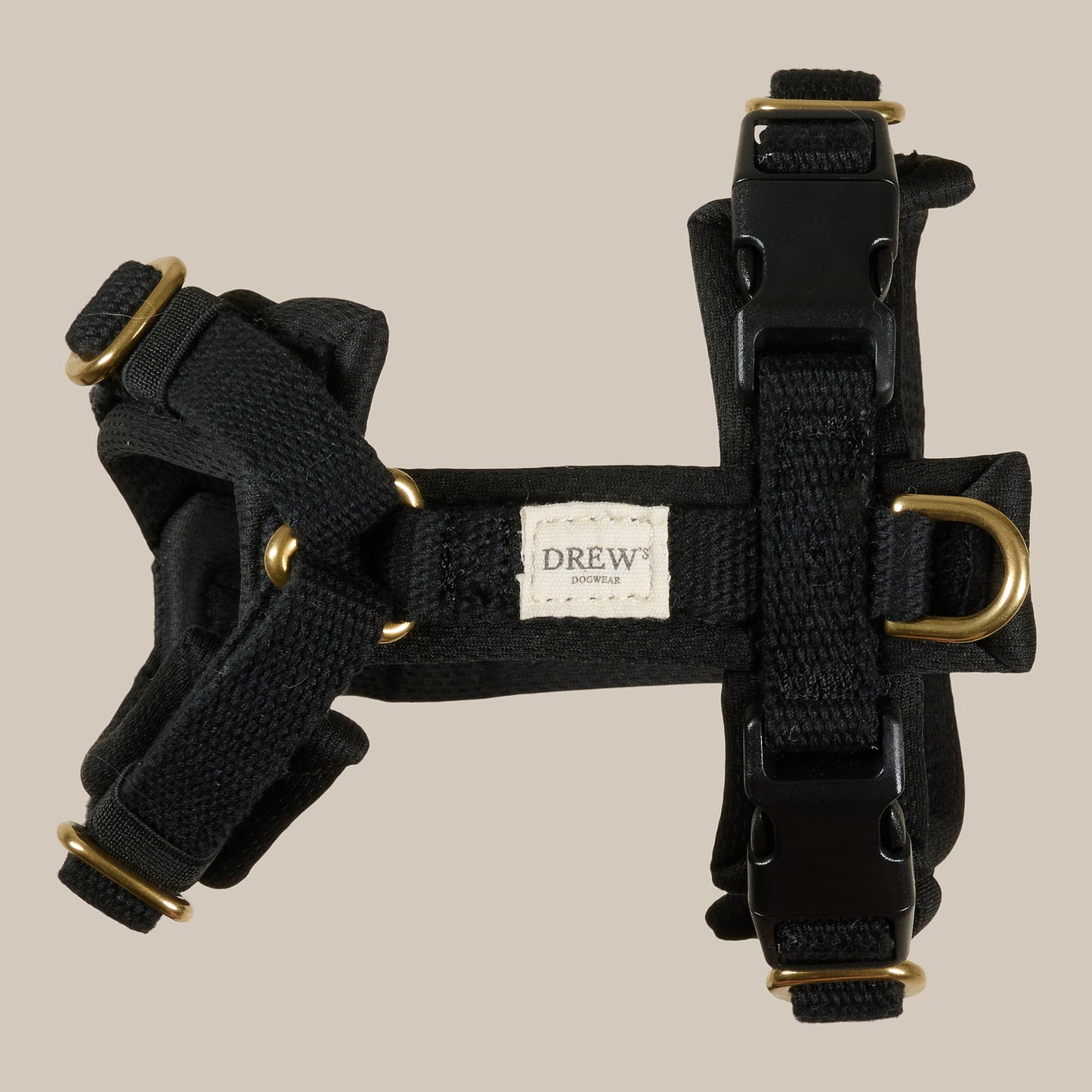 Black dog harness with gold hardware on a beige background