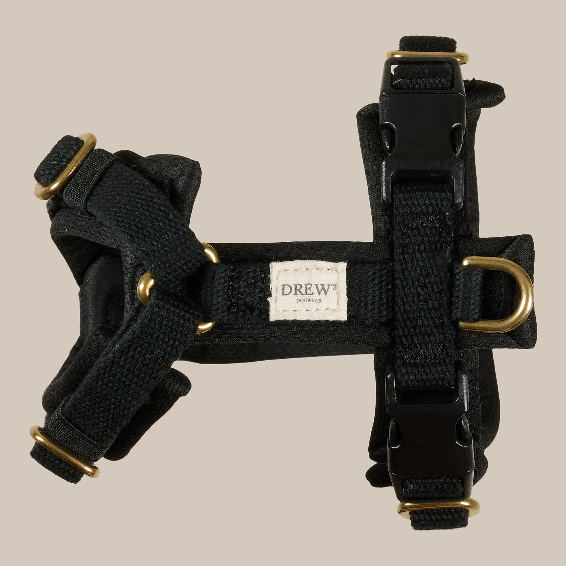 Black dog harness with gold hardware on a beige background