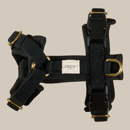 Black dog harness with gold hardware on a beige background