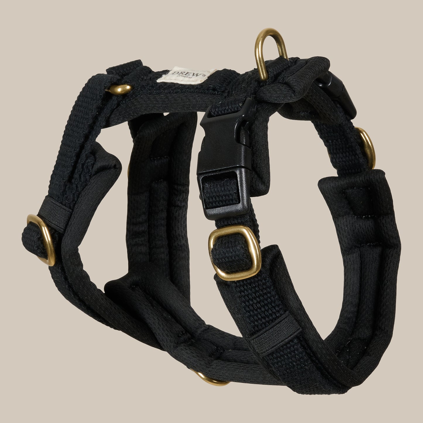Black dog harness with gold hardware on a beige background