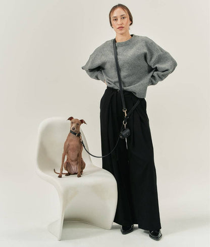 Person wearing a gray sweater and black pants standing next to a small dog on a white chair.