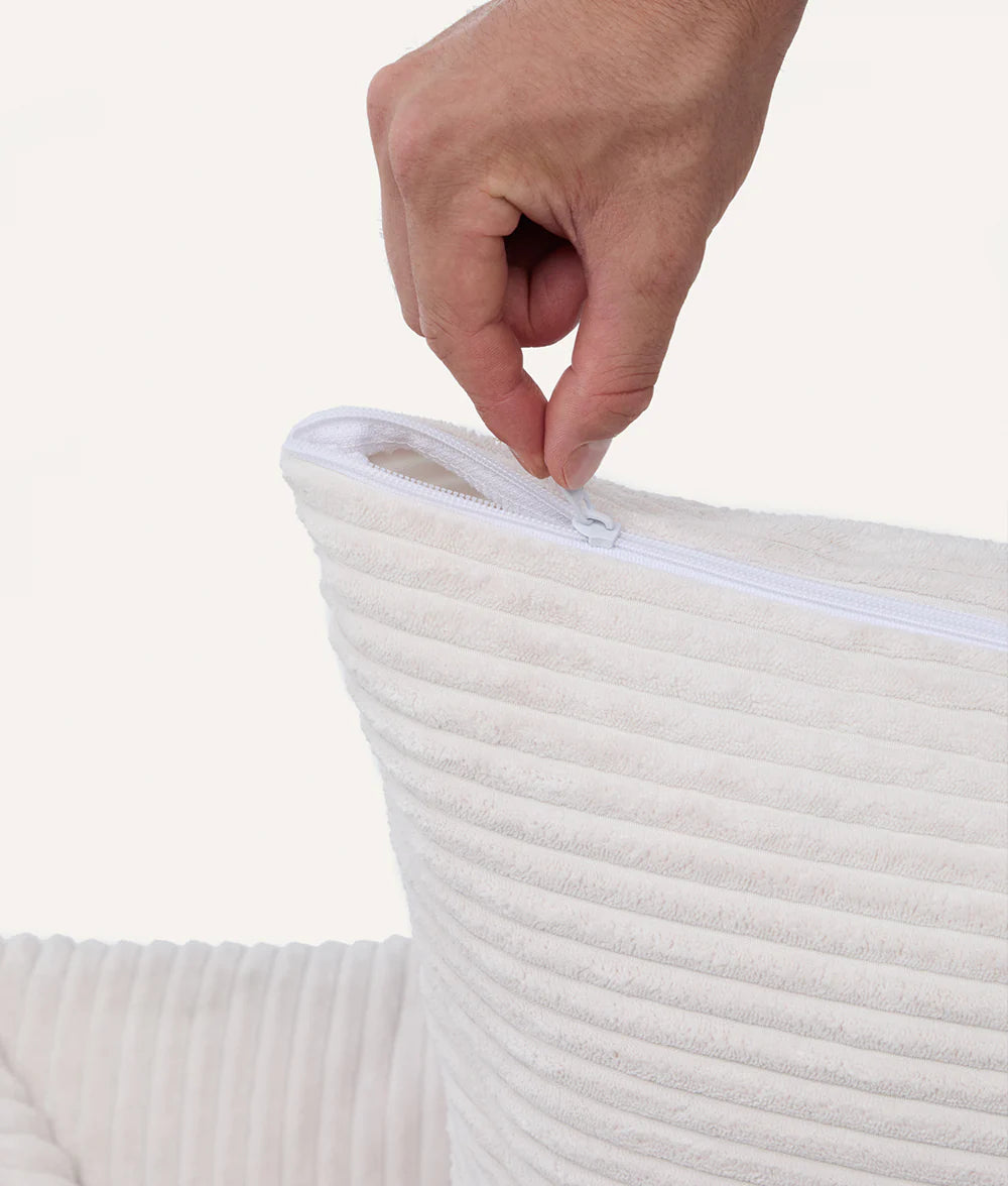 Hand zipping a white corduroy bag against a light gray background