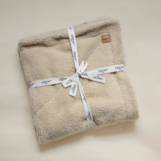 Folded beige sherpa blanket with 'Drew' branding on a light background