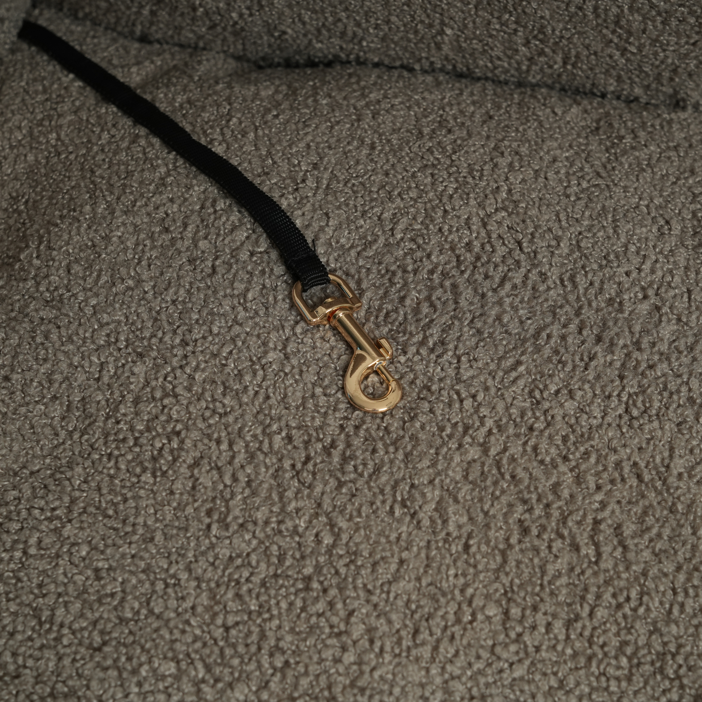 Close-up of a textured fabric surface with a gold clasp on a black cord.