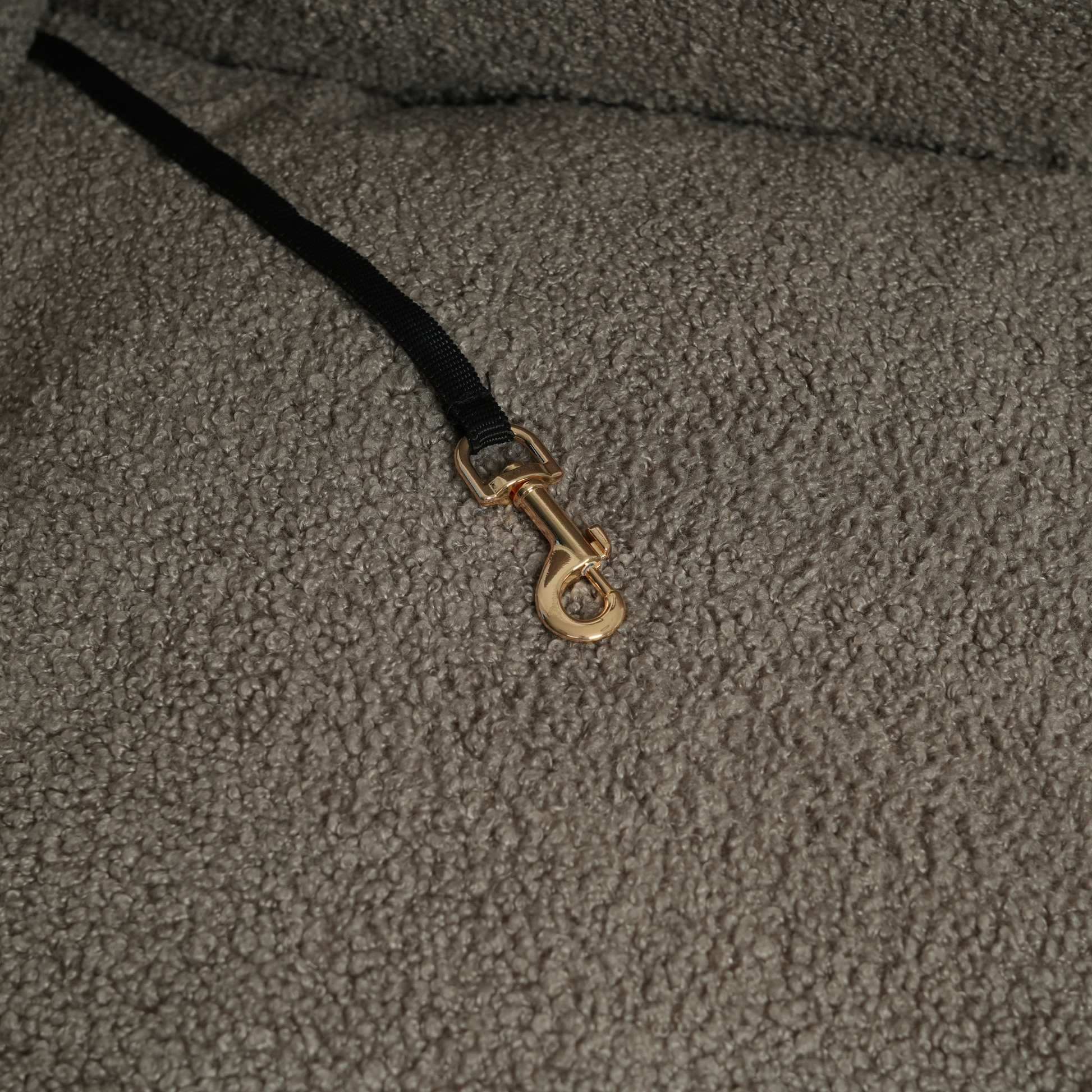 Close-up of a textured fabric surface with a gold clasp on a black cord.