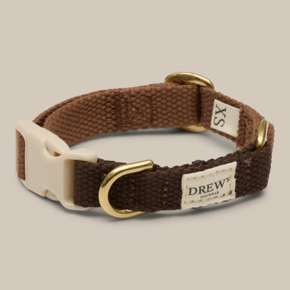 Brown dog collar with gold hardware and a label on a beige background