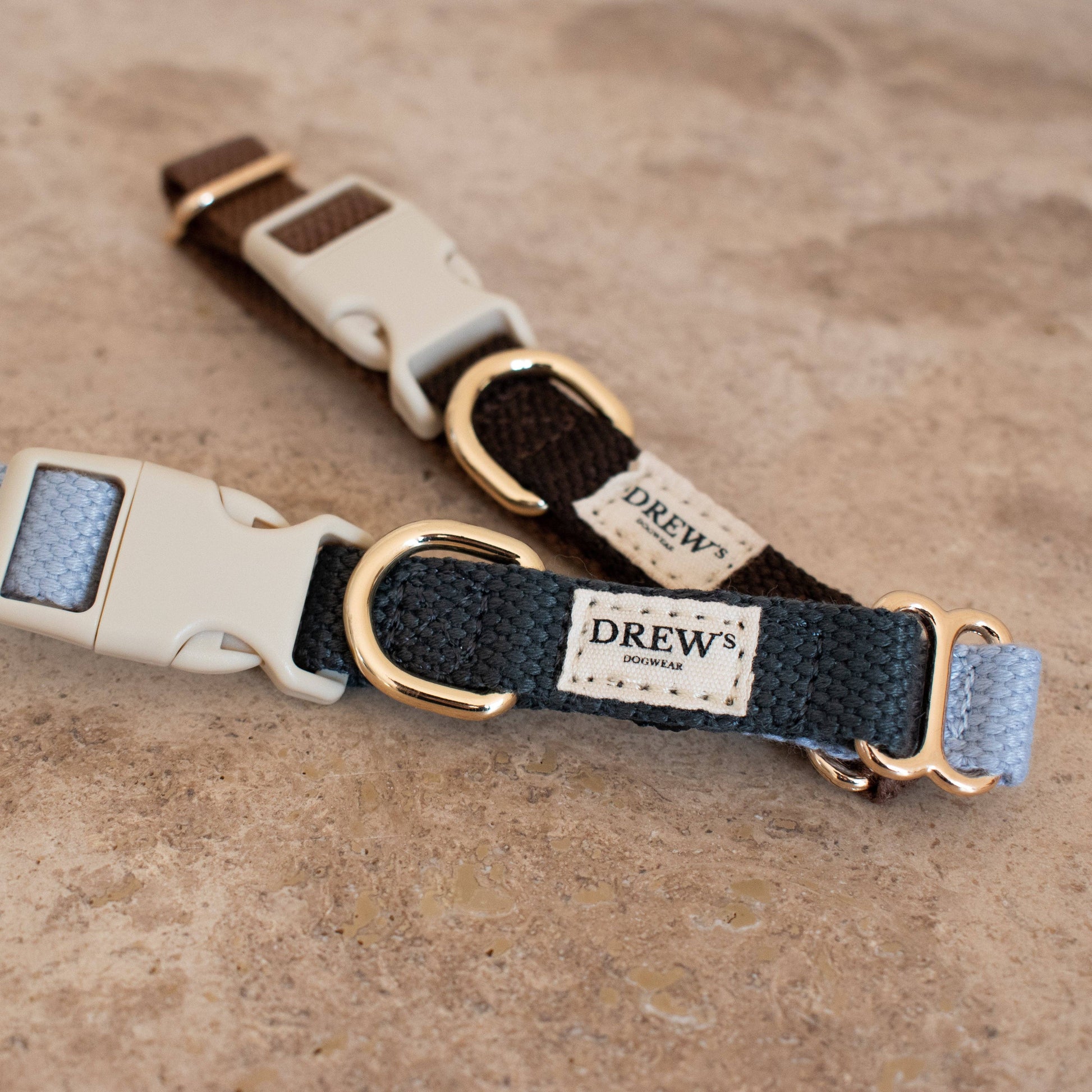 Two dog collars with gold buckles on a beige surface, featuring the brand 'Drew'.