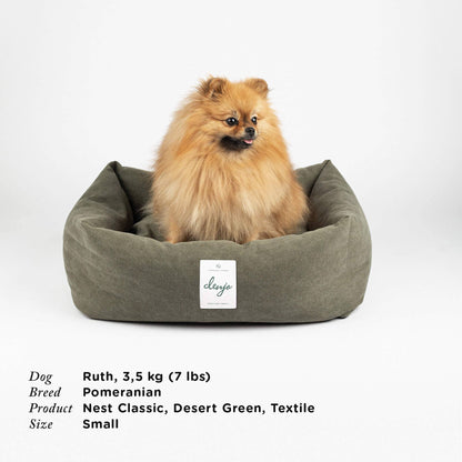 Pomeranian dog in a desert green pet bed with 'Clevage' label on a white background