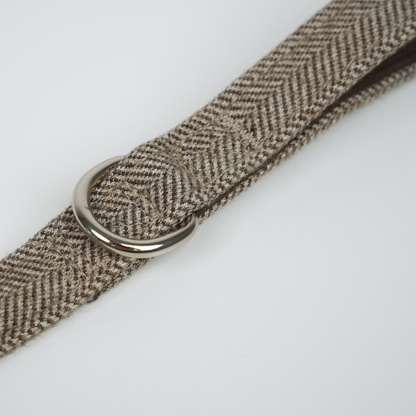 Brown herringbone patterned belt with a silver buckle on a white background