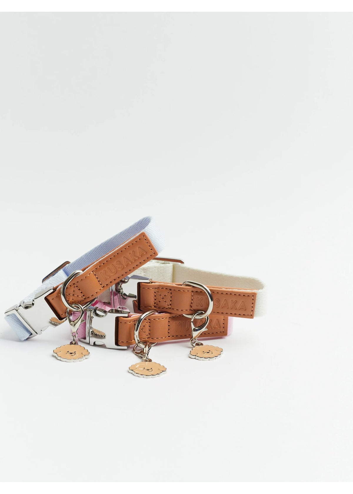 A set of dog collars with tan leather straps, silver buckles, and hanging dog-shaped charms, displayed on a clean white background.