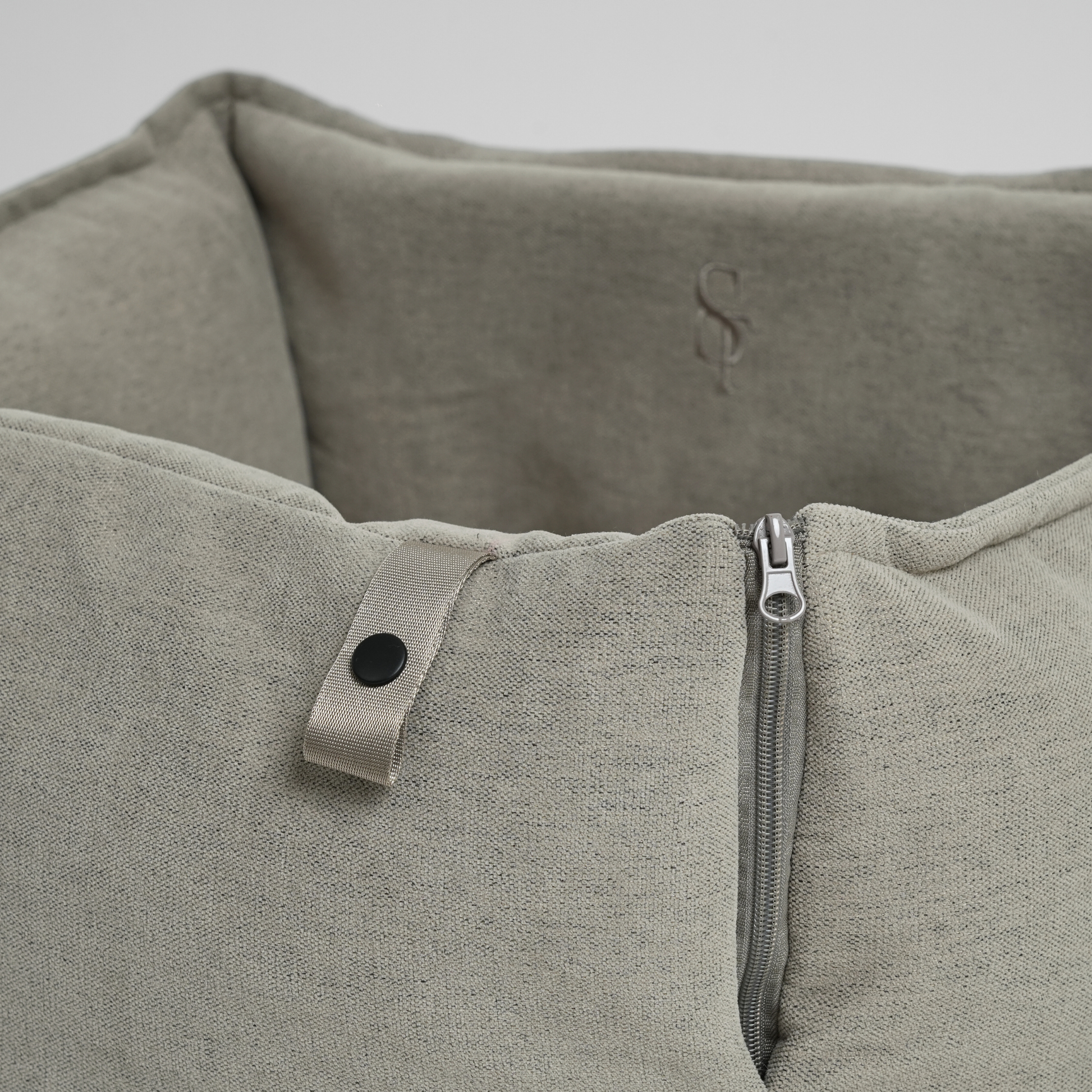 Close-up of a textured gray dog car seat with a zipper and button detail on a light gray background.