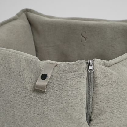 Close-up of a textured gray dog car seat with a zipper and button detail on a light gray background.
