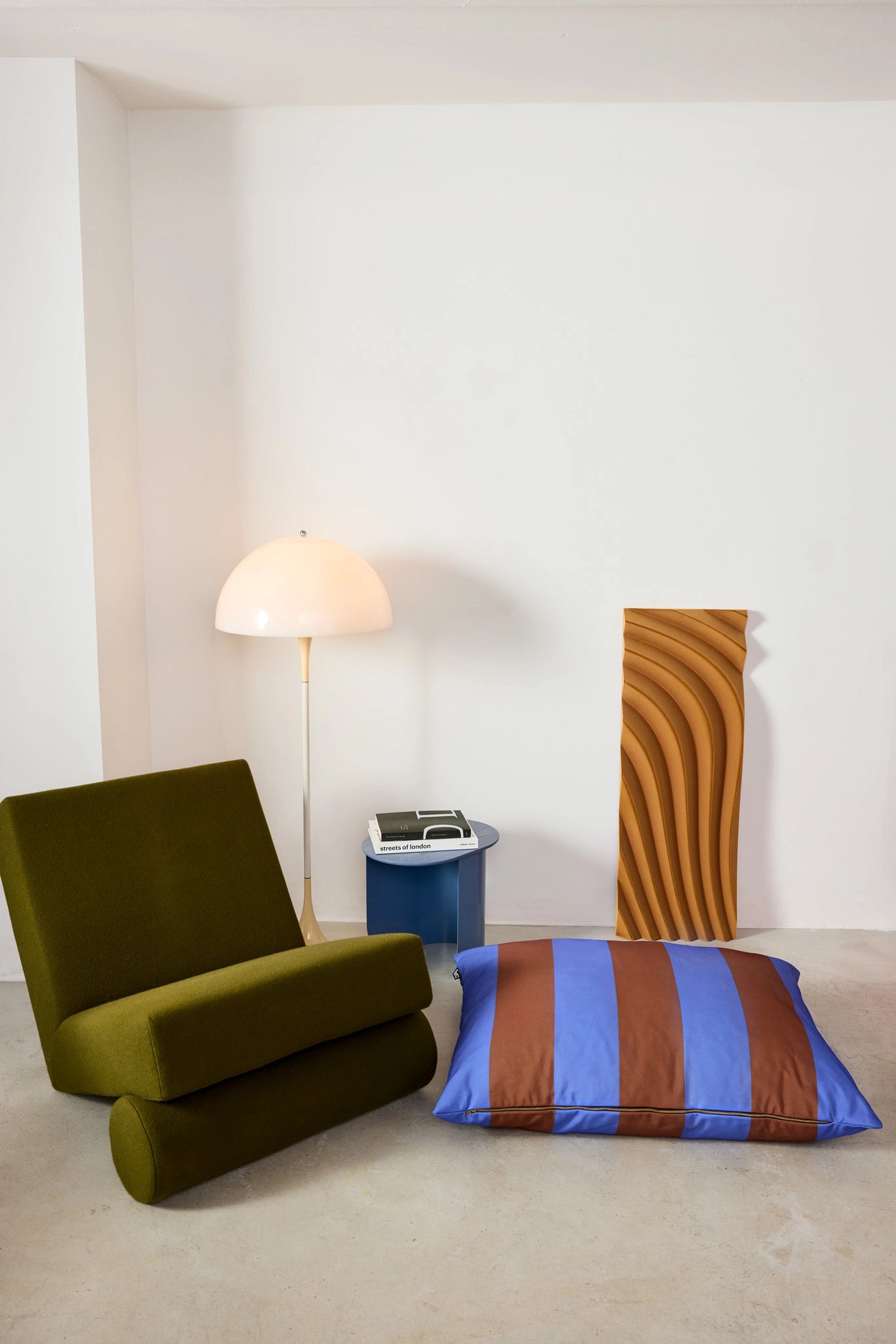 Modern green chair with a striped pillow and a lamp in a minimalistic room.