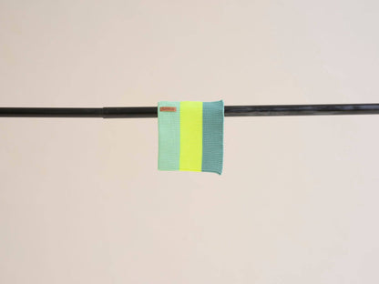 Two green and yellow striped fabric bands on a black rod against a beige background