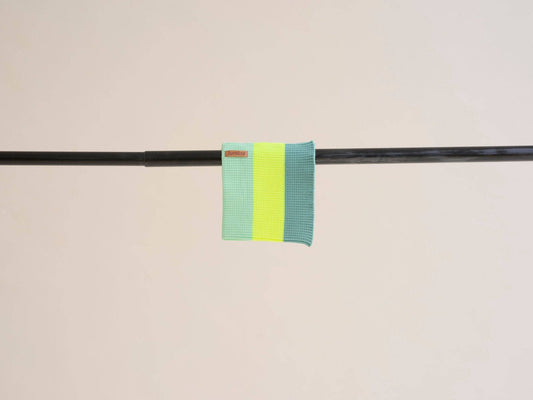 Two green and yellow striped fabric bands on a black rod against a beige background