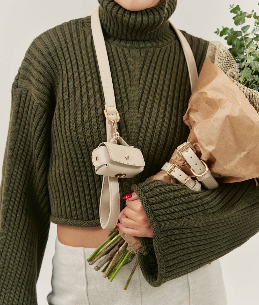 Person wearing a green ribbed sweater holding a beige handbag and bouquet of flowers.