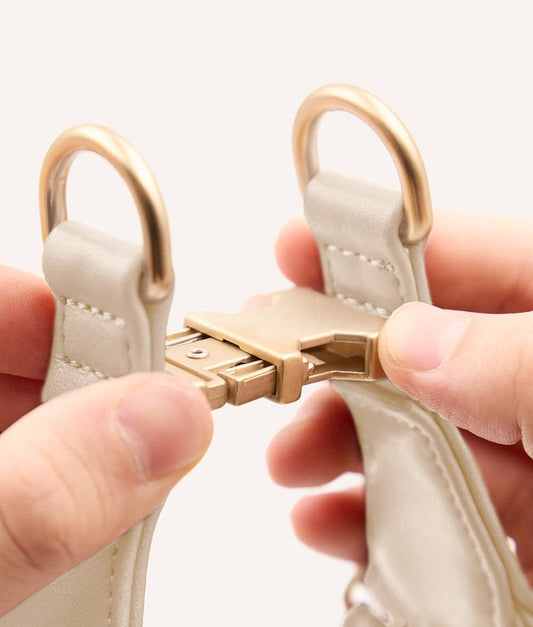 Close-up of a beige handbag with gold hardware being held by a person's fingers.