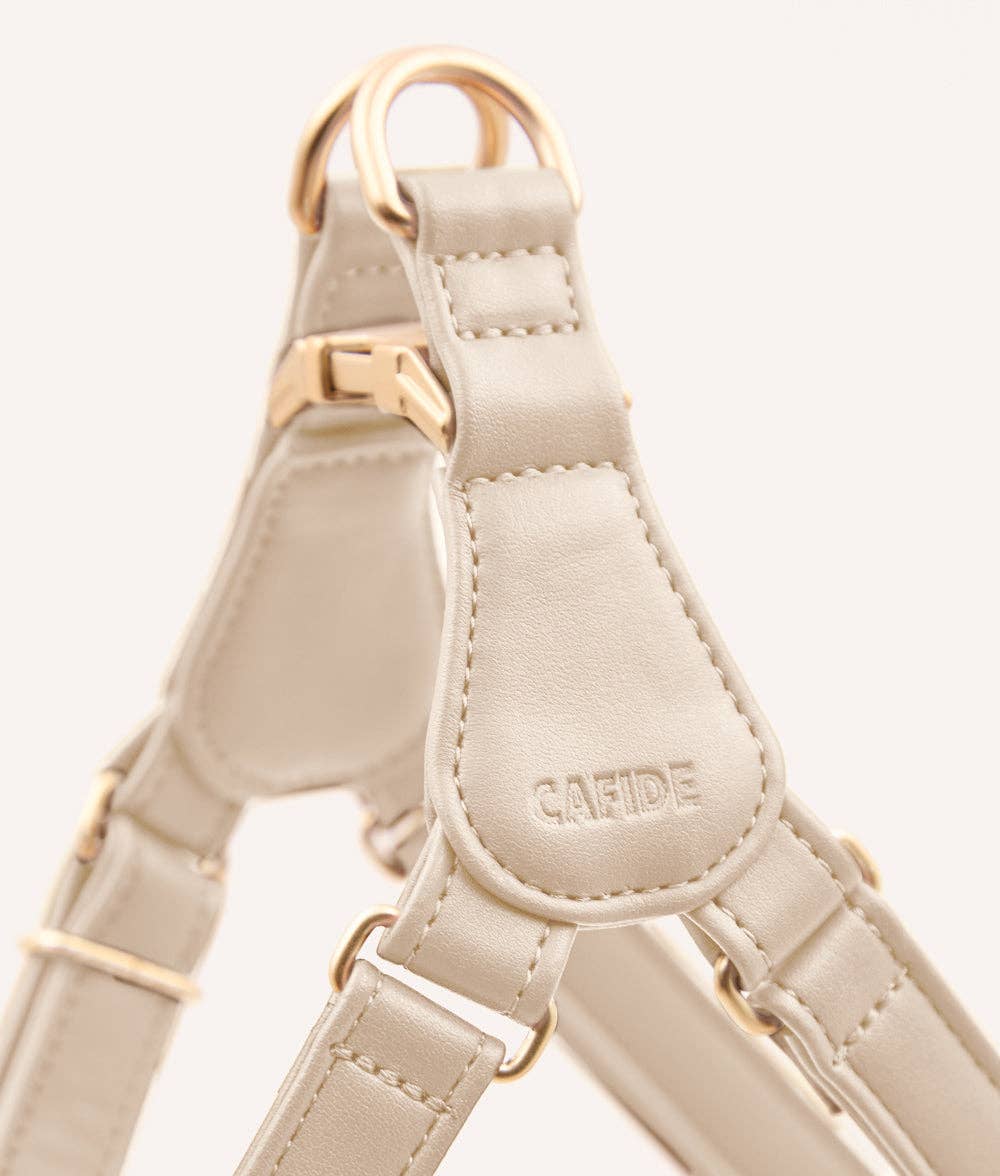 Beige dog harness with gold hardware on a light gray background