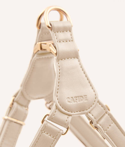 Beige dog harness with gold hardware on a light gray background