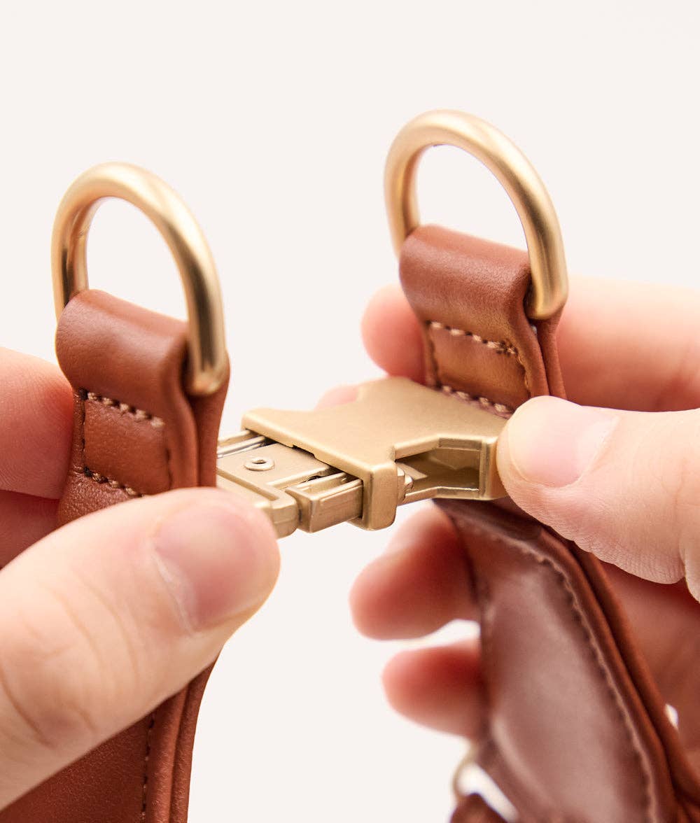 Brown leather keychain with gold clasp held by a hand against a white background