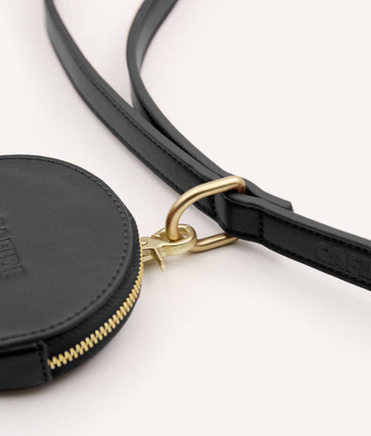 Black circular pouch with gold zipper and strap on a white background