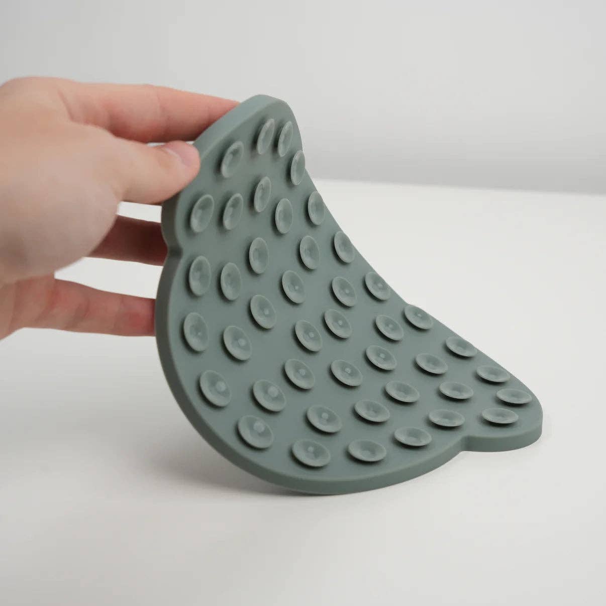 Green silicone mat with raised circular nodes held by a hand on a white background