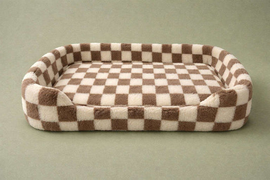 A plush rectangular pet bed with a brown and cream checkered pattern, shown on a solid muted green background.