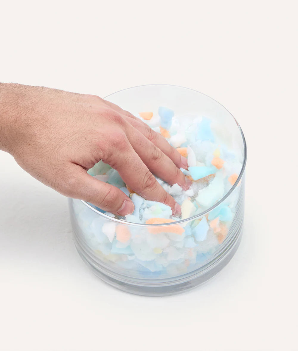 Hand interacting with colorful foam balls in a glass bowl on a white background