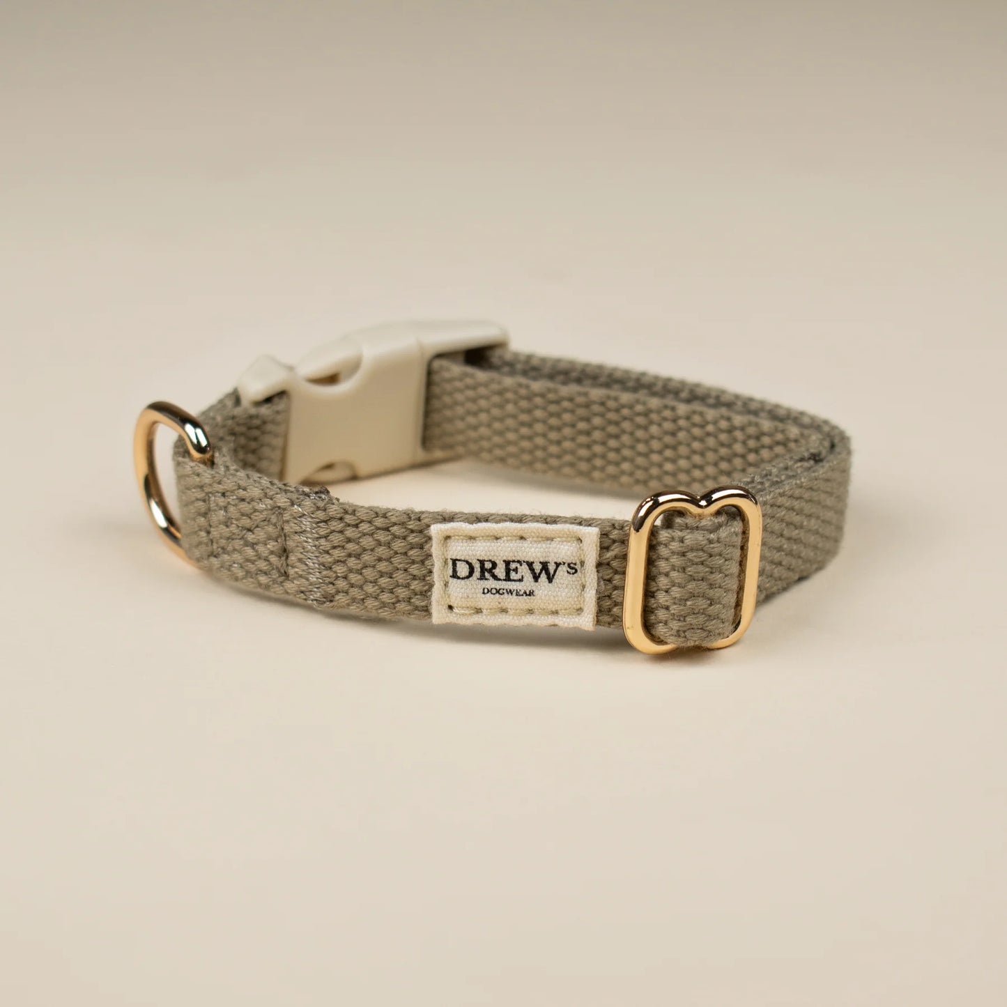 Dog collar with gold buckle and 'Drew' label on a beige background