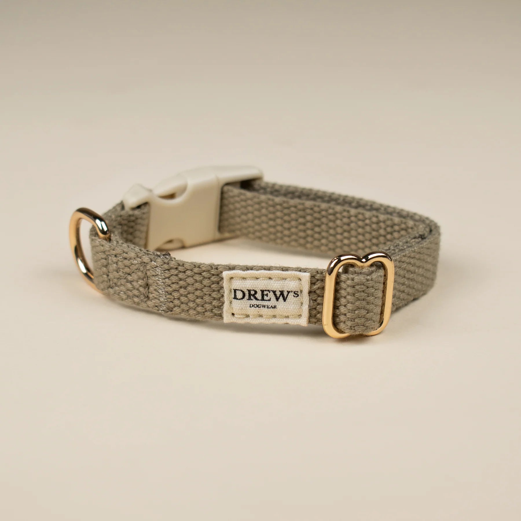 Dog collar with gold buckle and 'Drew' label on a beige background