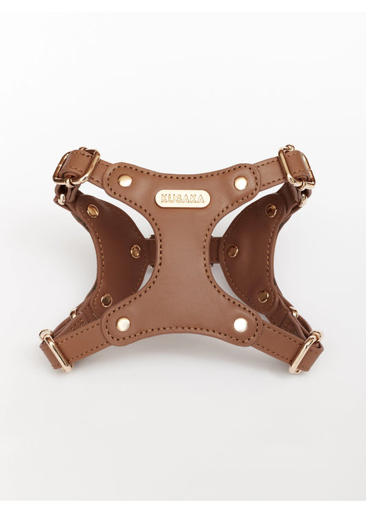 A brown faux-leather dog harness with gold-tone hardware and a central metal plaque engraved with the brand name 'KIKARA', shown on a plain white background.