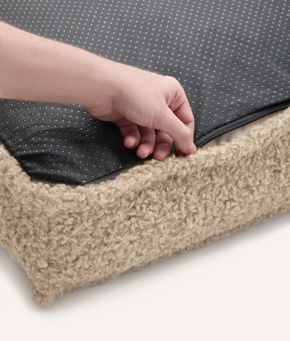 Hand zipping a black and gray fabric over a beige carpeted surface