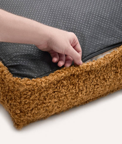 Hand opening a pet bed with a brown exterior and black interior.