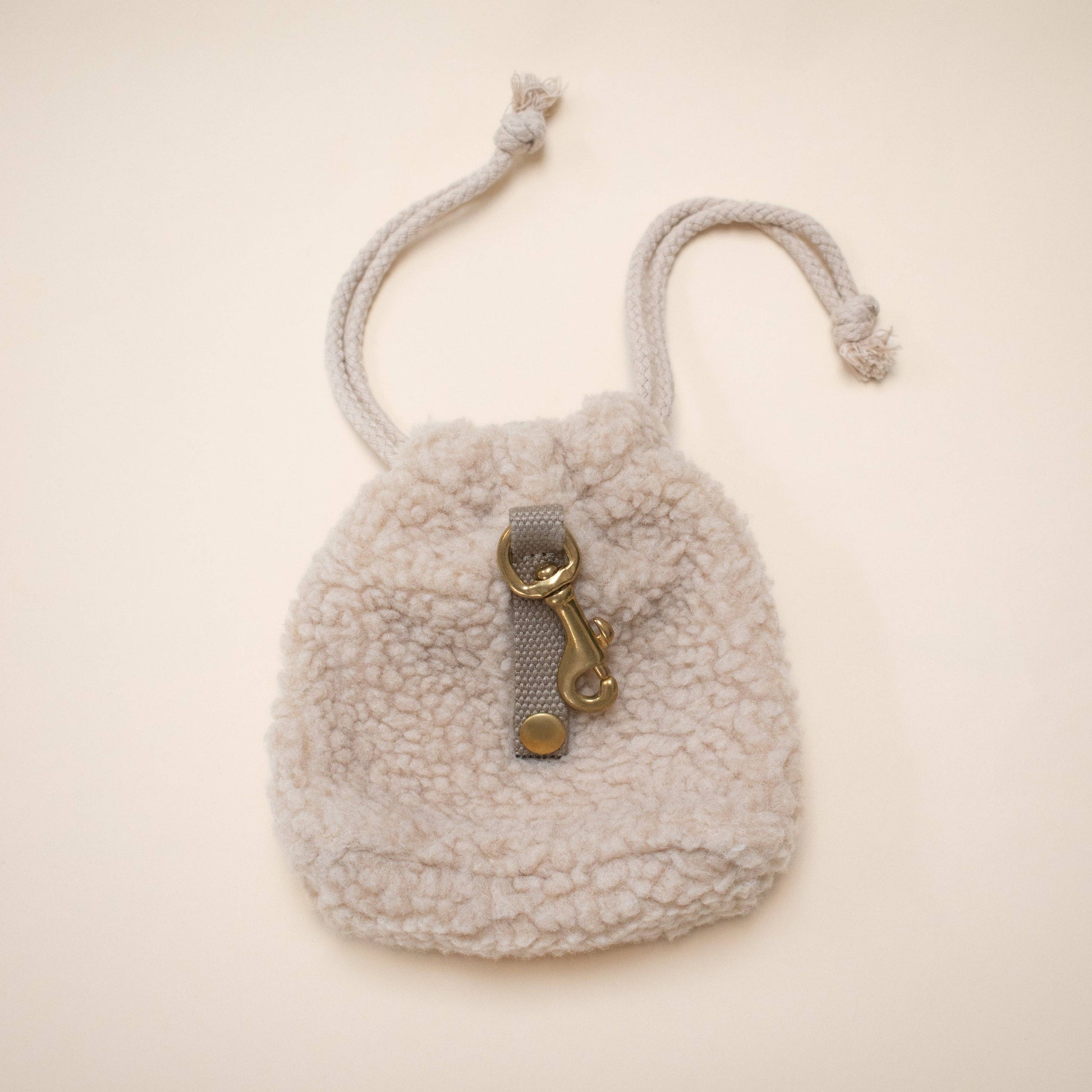 Small fluffy pouch with a drawstring and gold clasp on a beige background